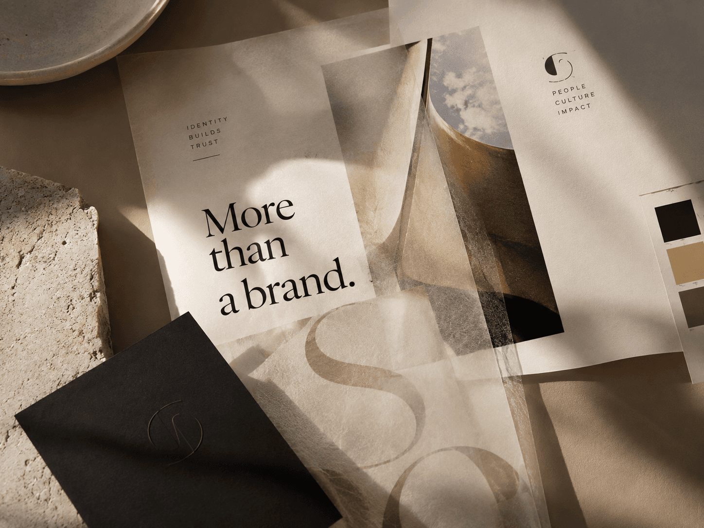 A printed card reading “More than a brand” among paper samples and stone, in warm light