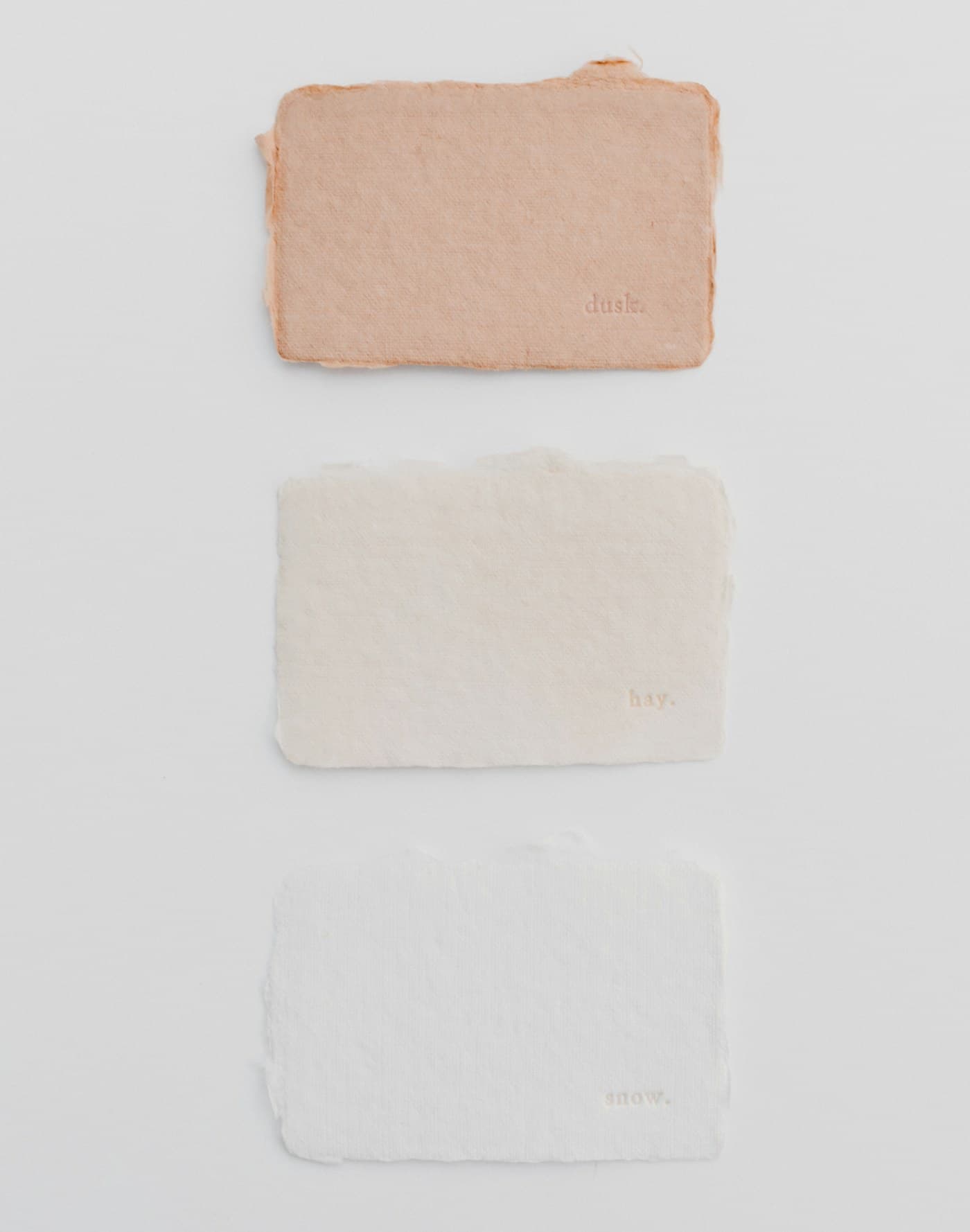 Three textured paper swatches — peach, cream and white — on a white surface