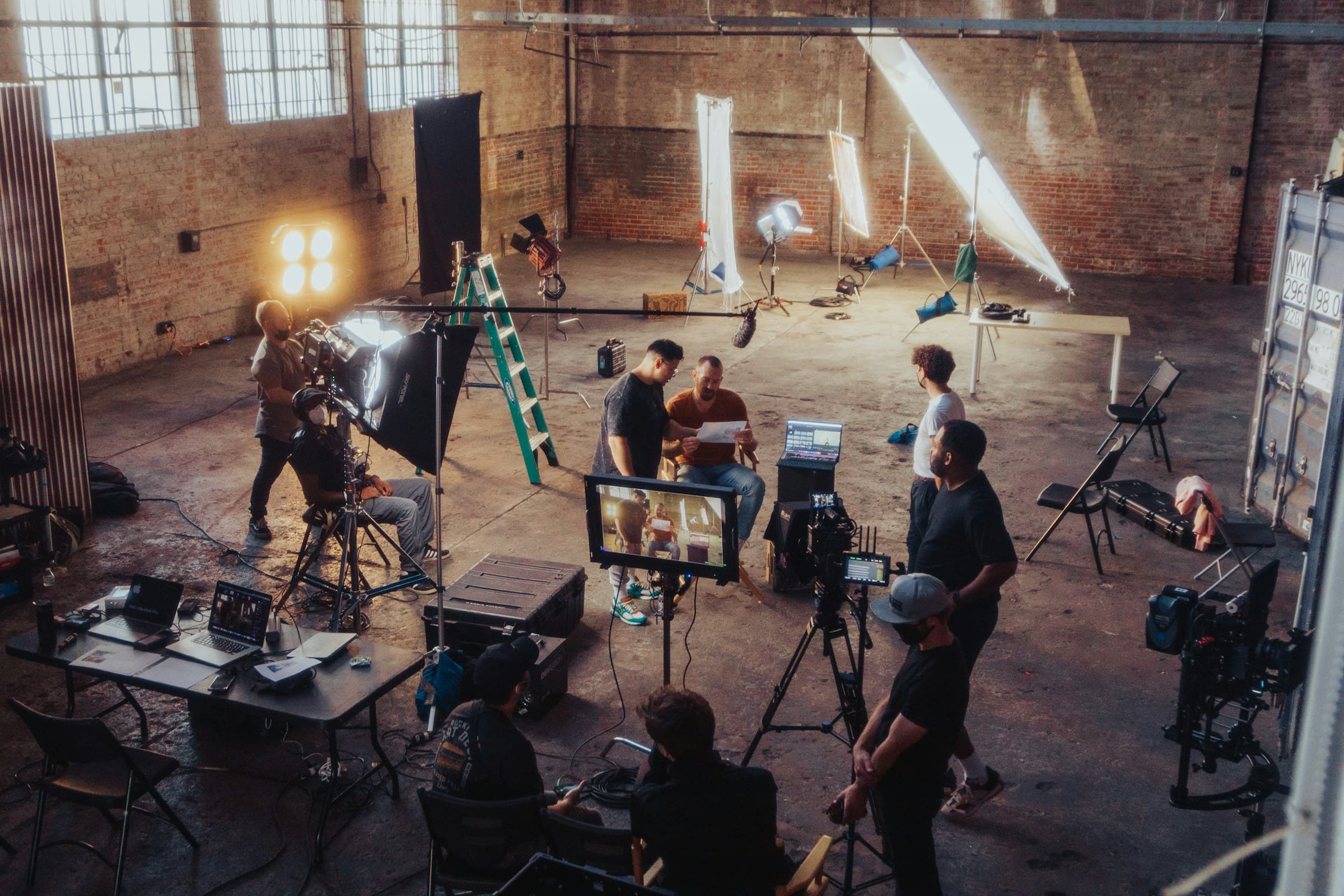 A film crew at work in a warehouse studio, among lights and monitors