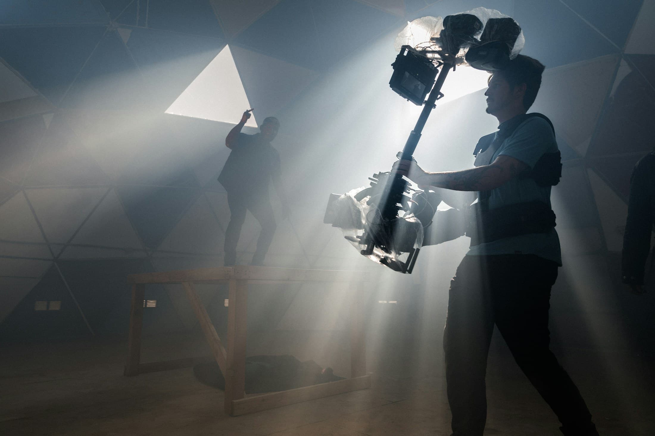 A camera operator with a rigged camera in a beam of light through haze, on a film set