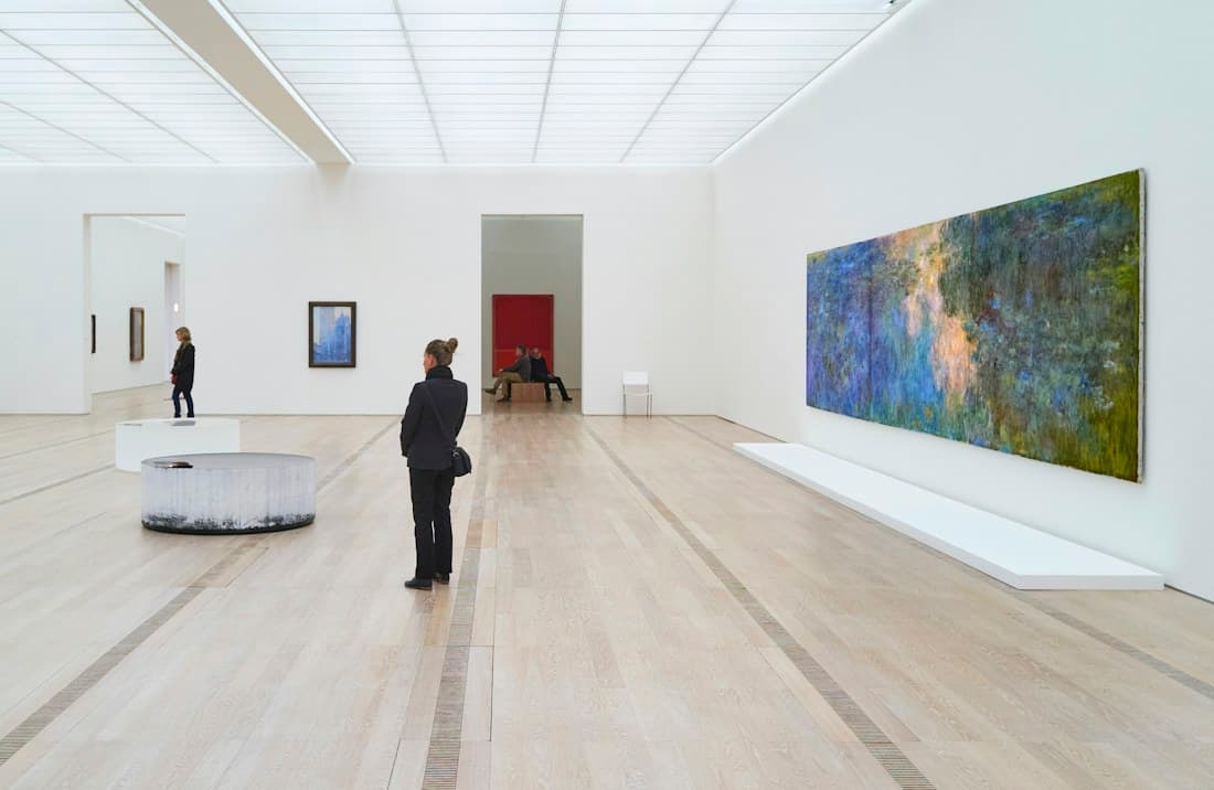 A visitor standing in a bright white gallery, looking at a large painting